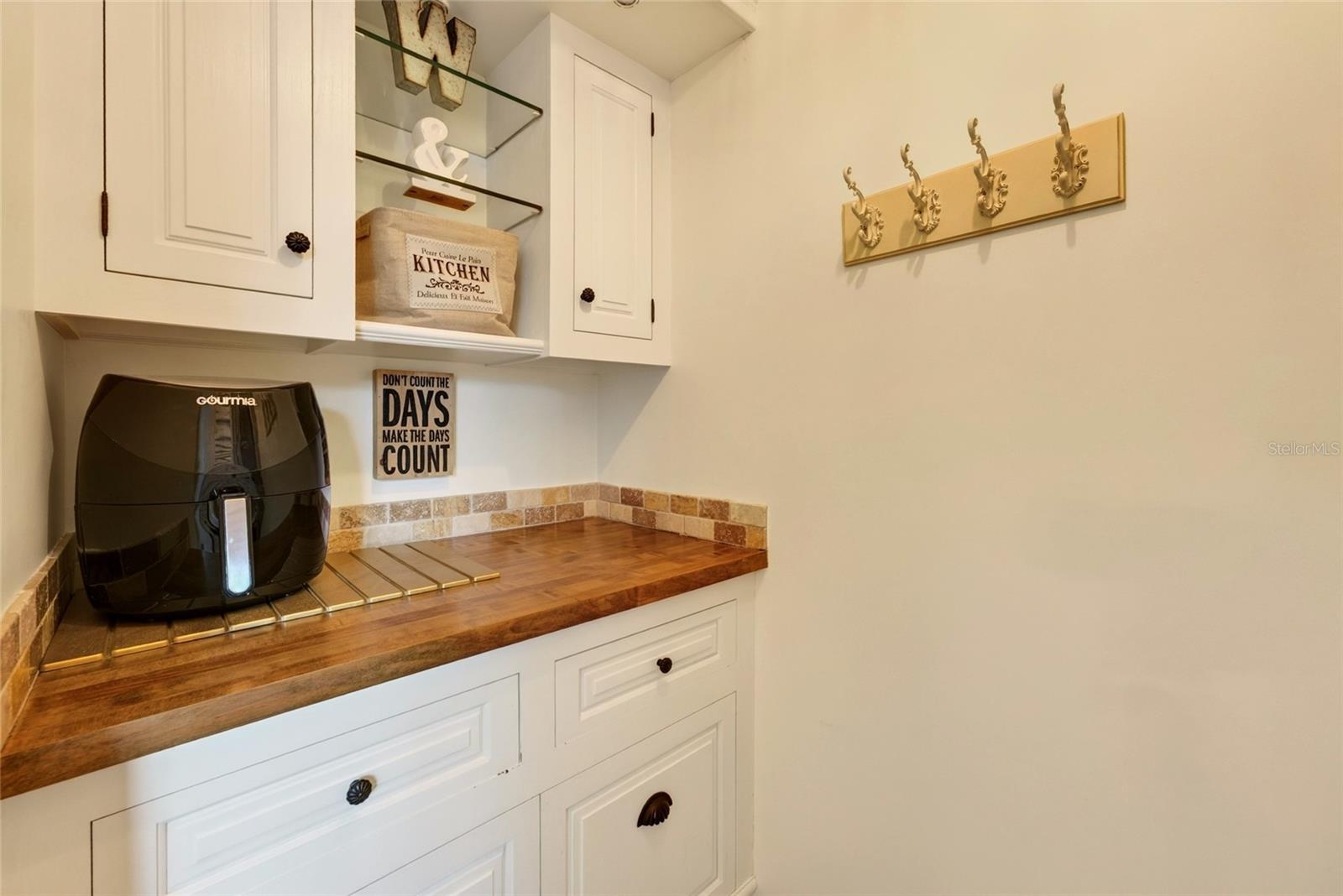 Kitchen coffee station with white cabinets, wood counter, black air fryer, and decorative wall hooks.