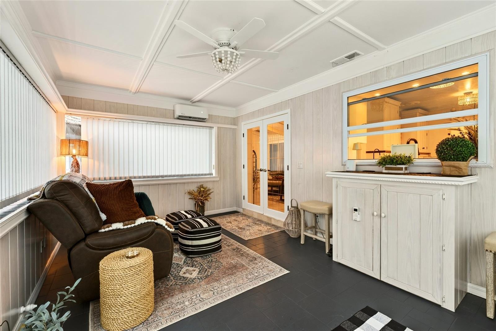 Furnished sunroom with a leather recliner, patterned rugs, and a pass-through counter to the kitchen.
