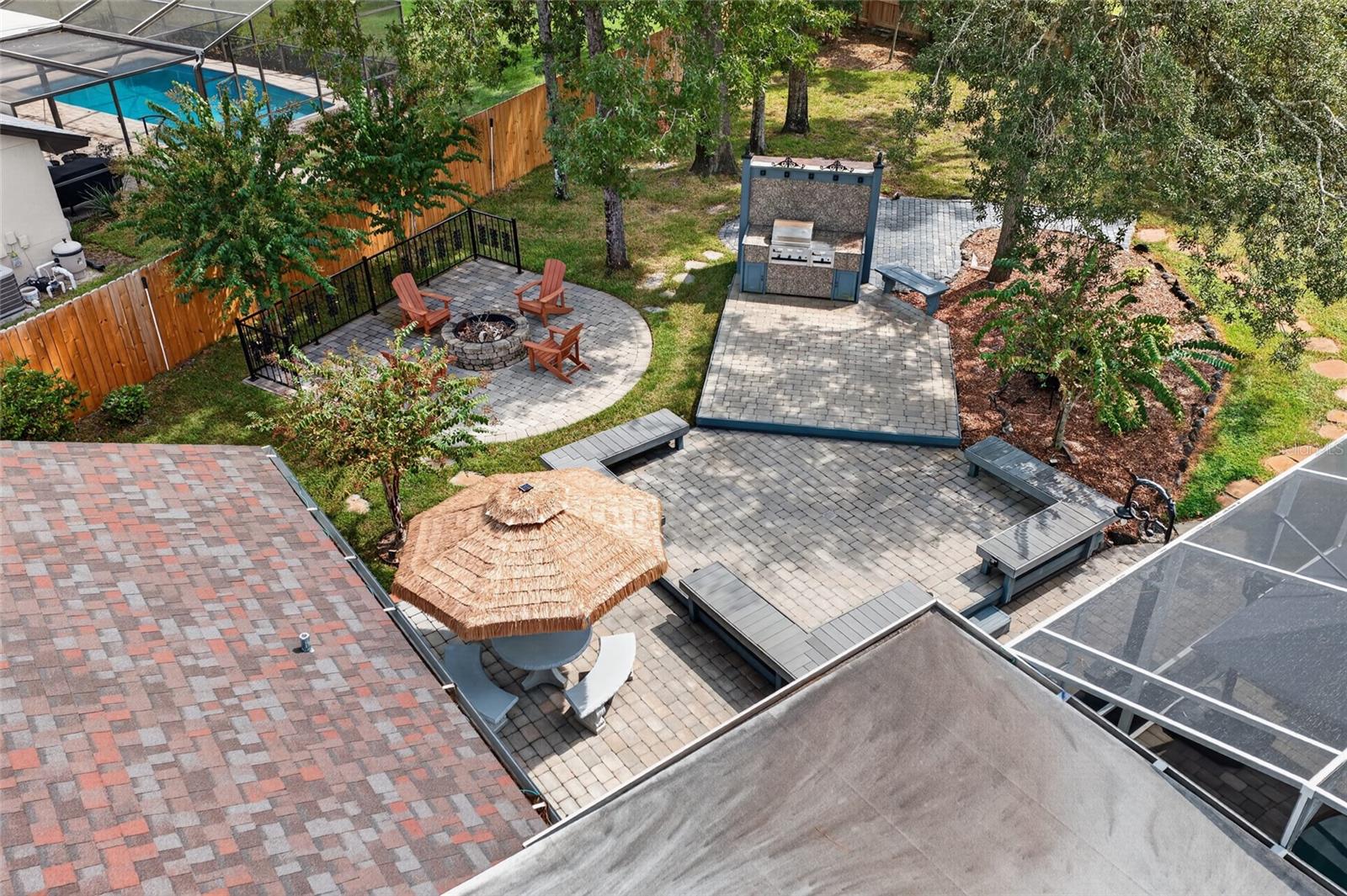 Aerial view of backyard patios with a fire pit, grill station, and screened pool enclosure.
