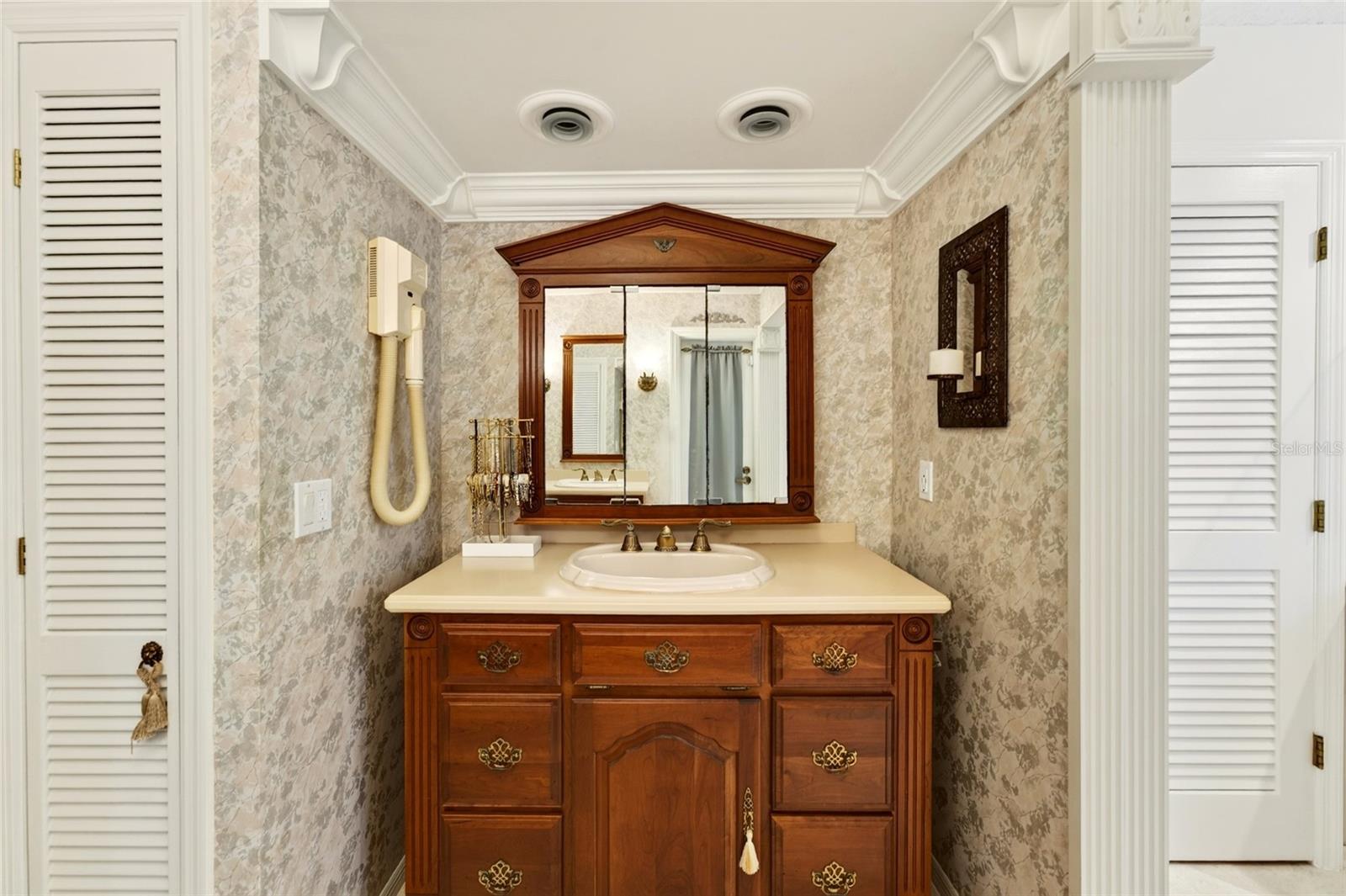 Bathroom vanity with an ornate dark wood cabinet, framed mirror, and cream countertop.