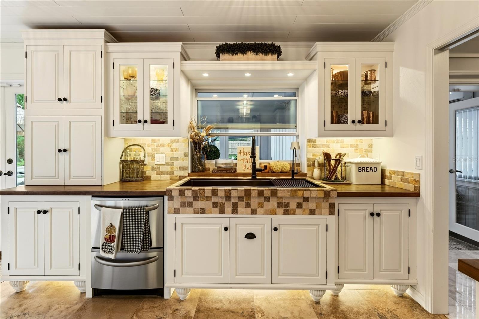 Kitchen with white cabinets, a tiled sink surround, dark wood counters, and a window above the sink.