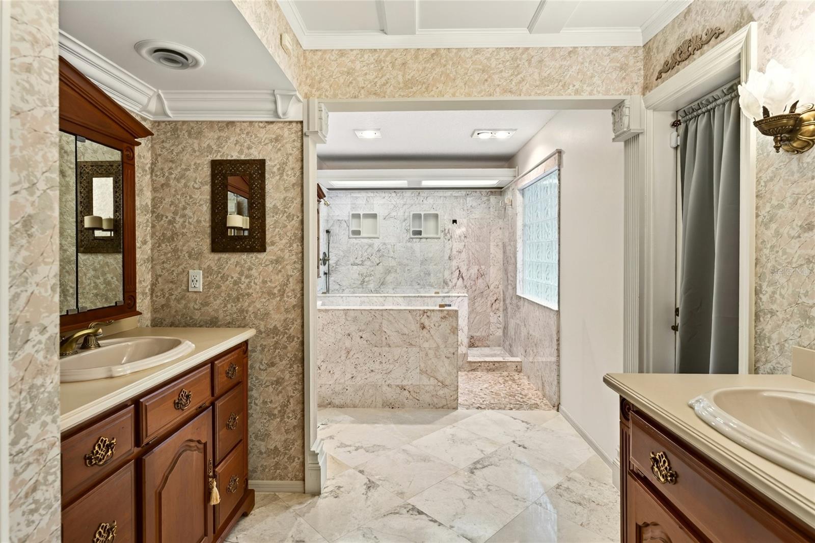 Marble bathroom with twin wood vanities and a large walk-in shower.