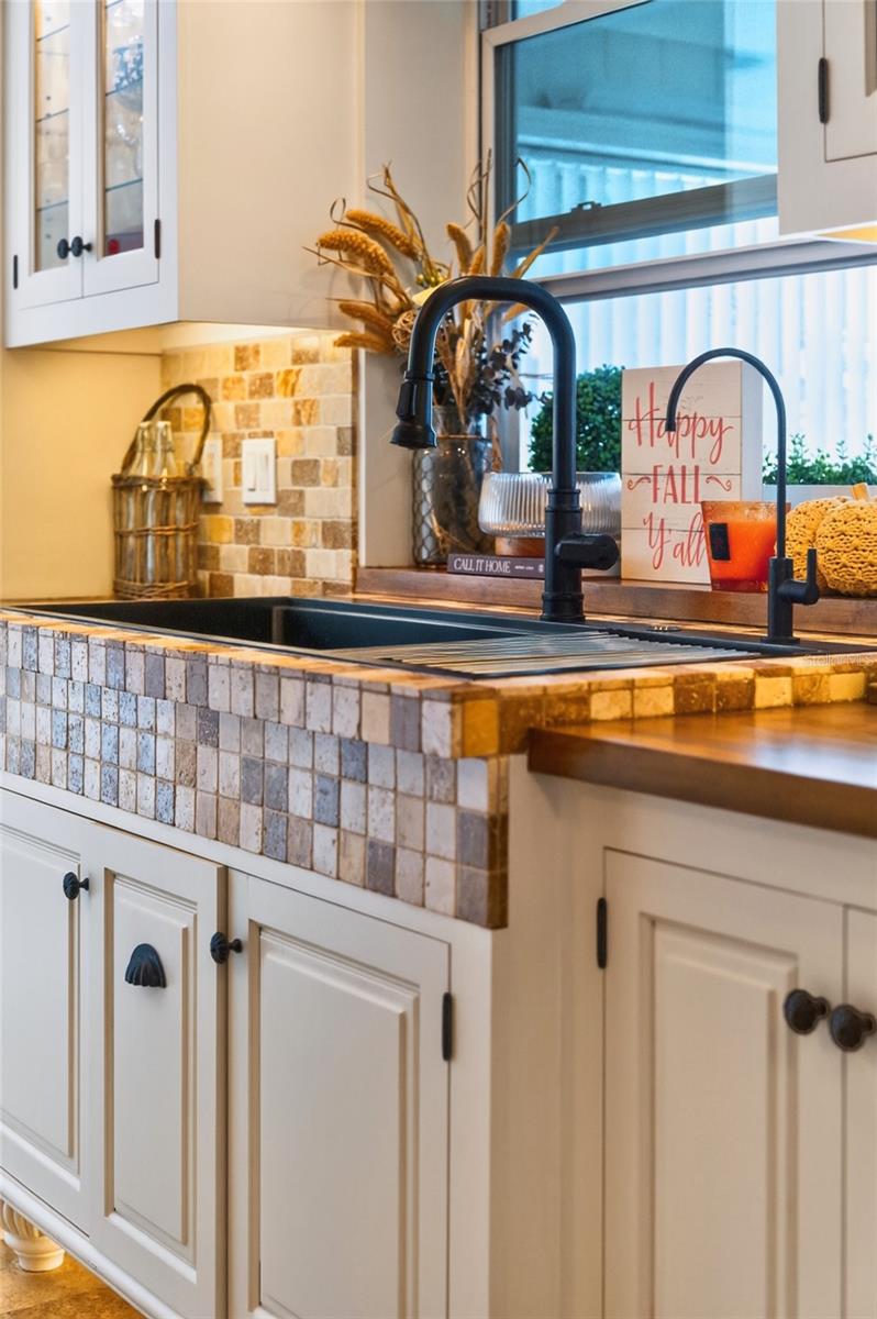 Kitchen sink with a multicolored tile surround, black faucet, cream cabinets, and fall decorations.