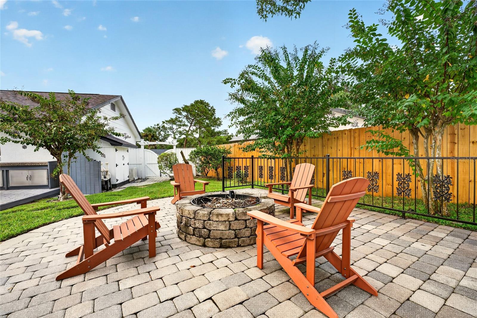 Backyard patio with a stone fire pit, Adirondack chairs, and a wooden privacy fence.