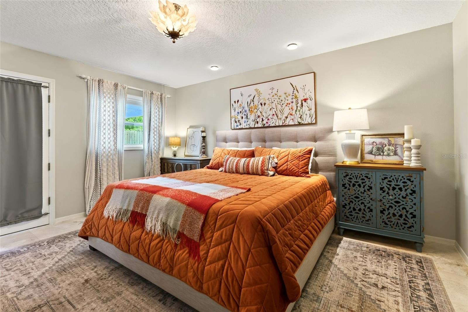 Bedroom with an orange quilted bed, tufted headboard, and floral artwork above it.
