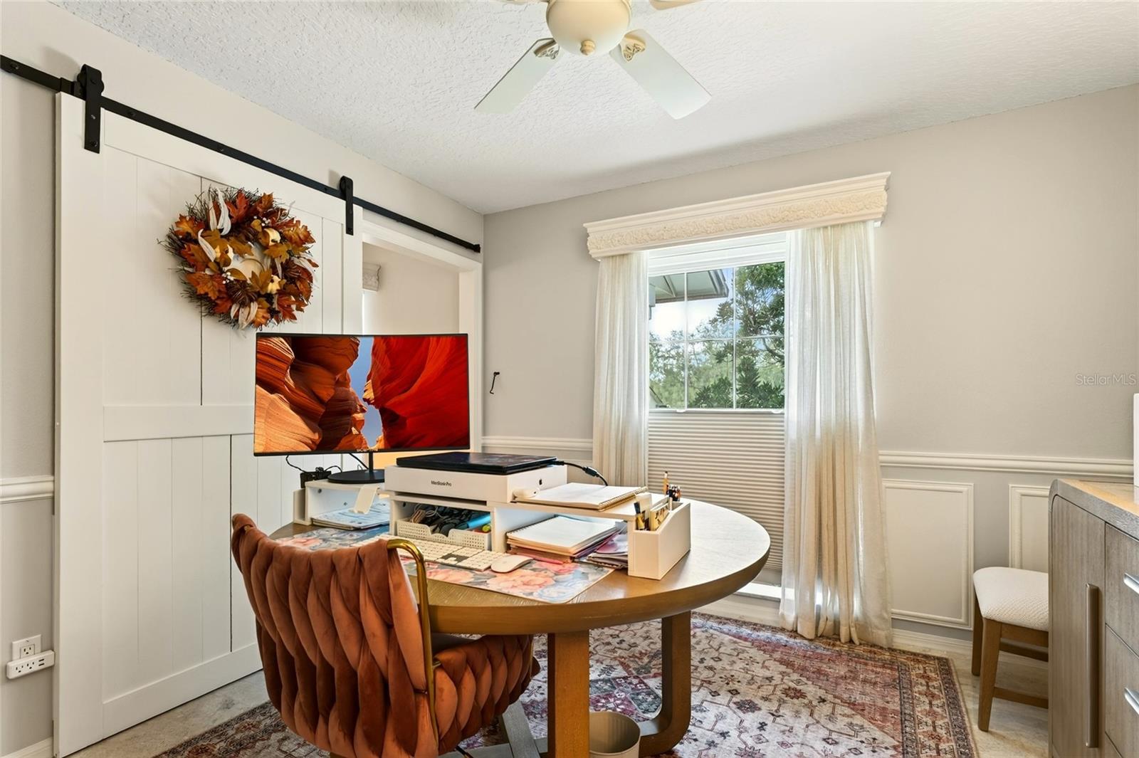 Furnished home office with a round desk, rust-colored chair, and white sliding barn door.
