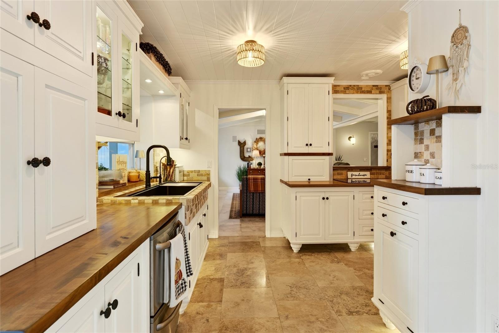 Kitchen with white cabinetry, butcher-block counters, black farmhouse sink, and patterned tile backsplash.