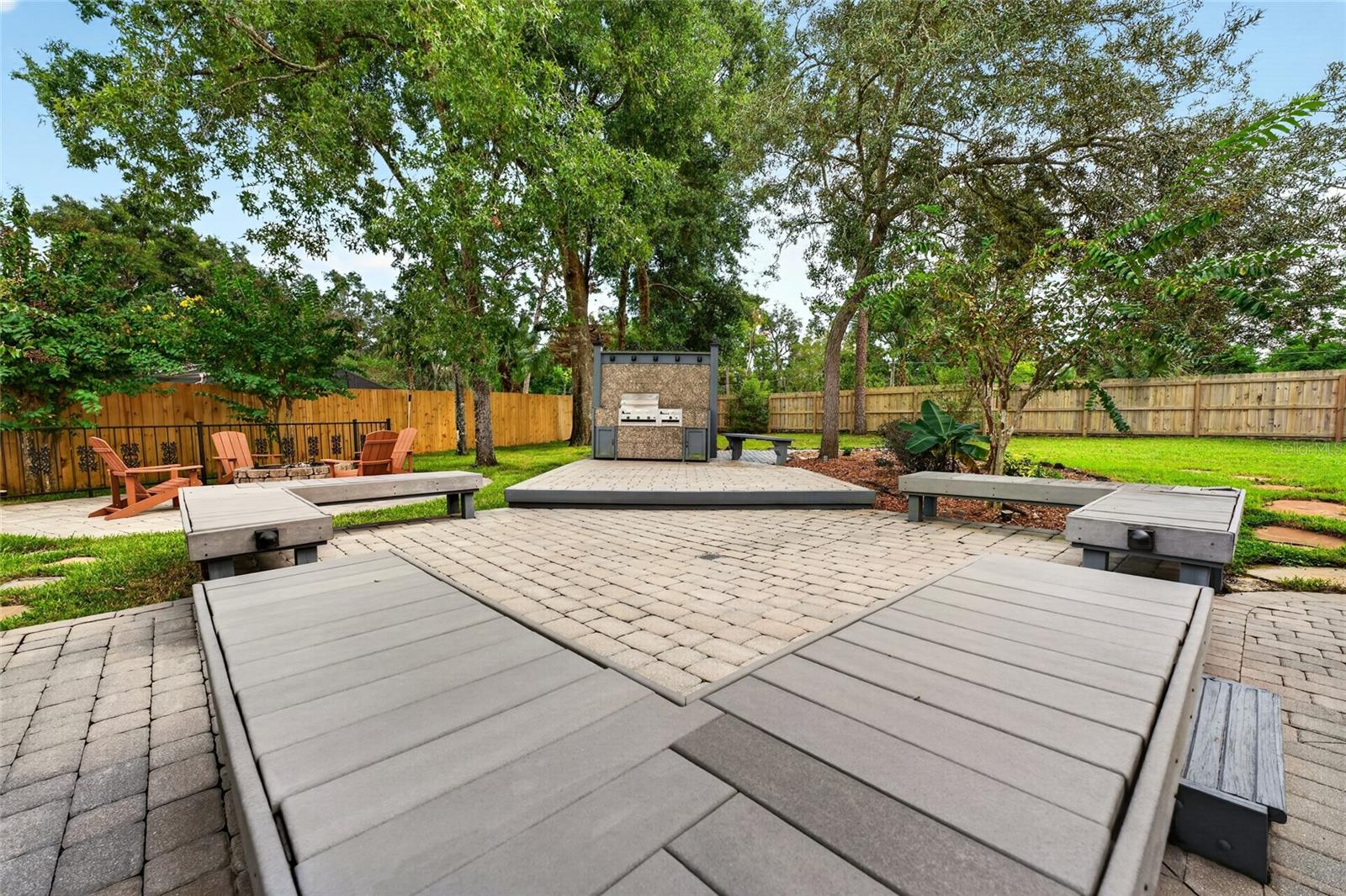 Backyard patio with a built-in outdoor kitchen, paver seating area, and mature trees.