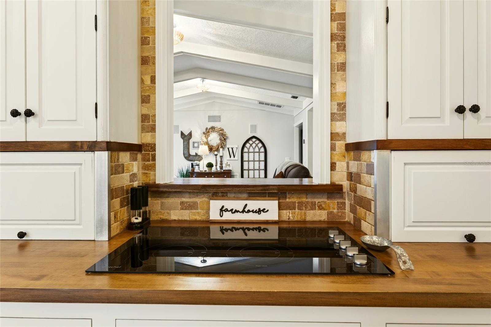 Kitchen with a black cooktop, wood countertops, white cabinets, and brick backsplash.