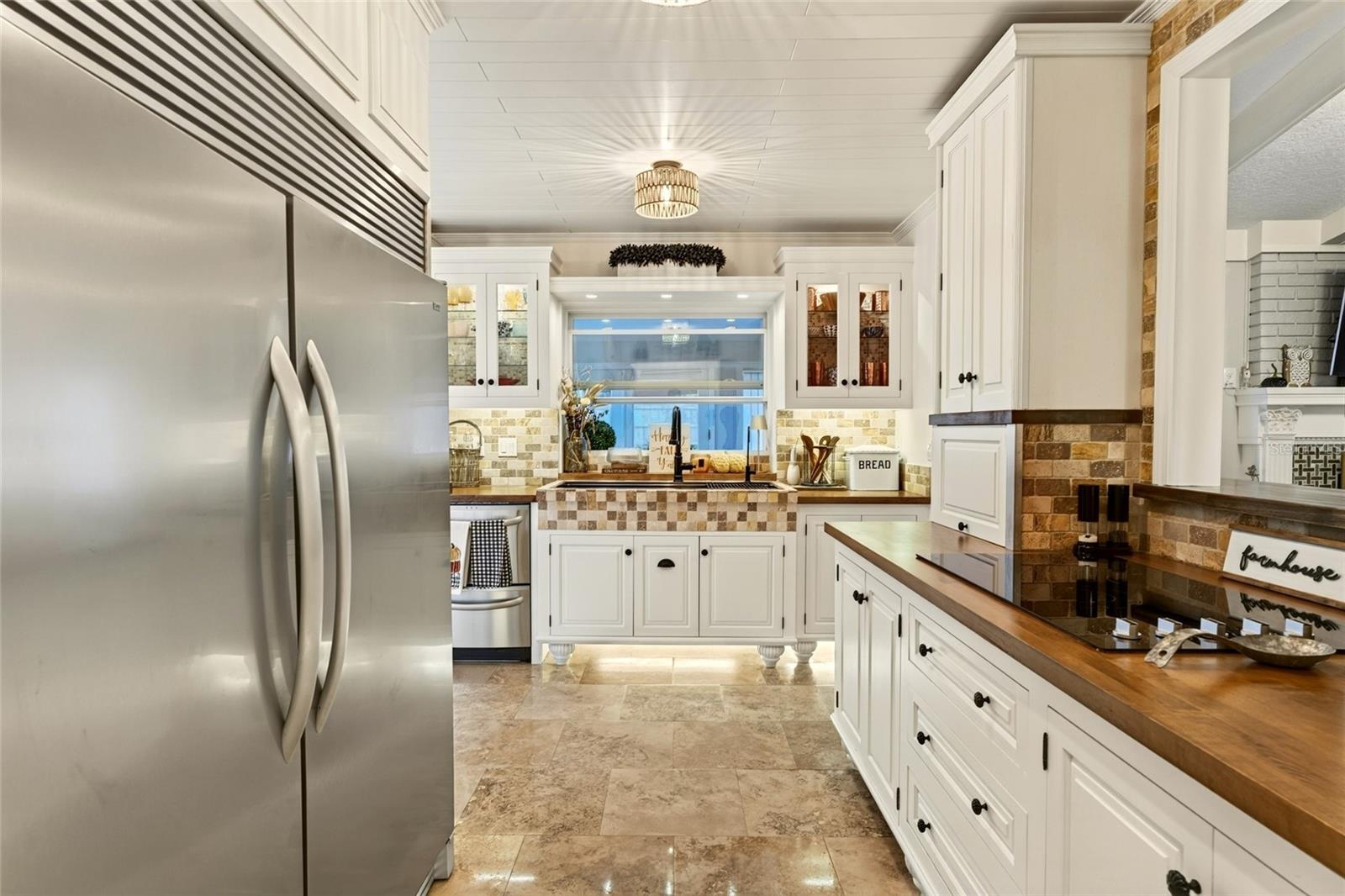 Bright kitchen with white cabinets, a stainless-steel refrigerator, wood countertops, and patterned tile backsplash.