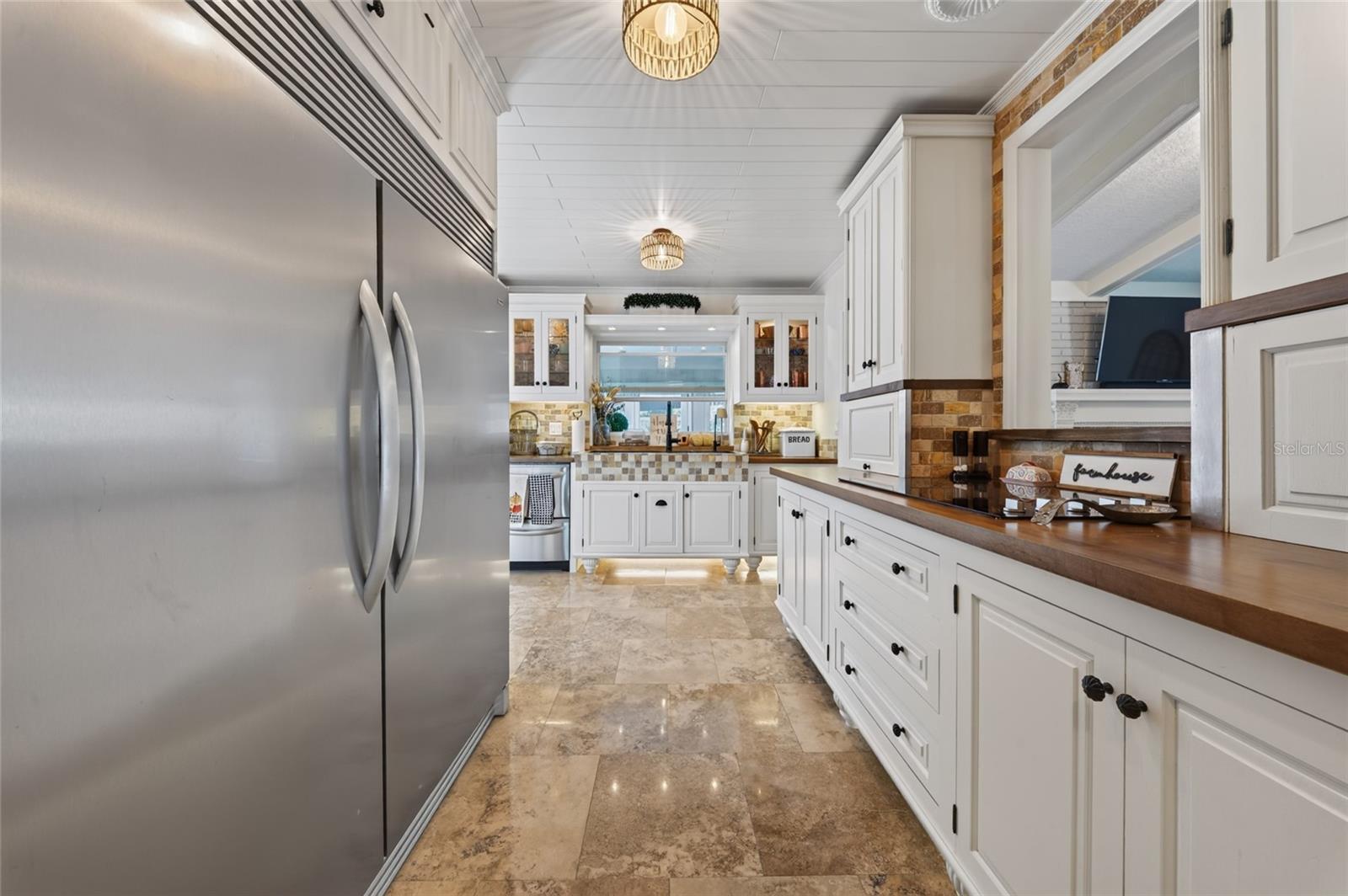 Kitchen with white cabinets, wood countertops, stainless-steel refrigerator, and brick backsplash.