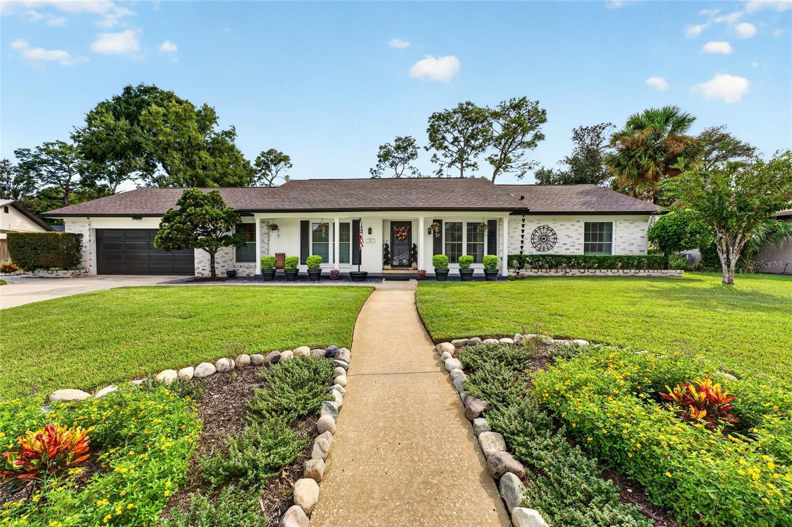 Single-story white brick home with a curved walkway through landscaped flower beds.