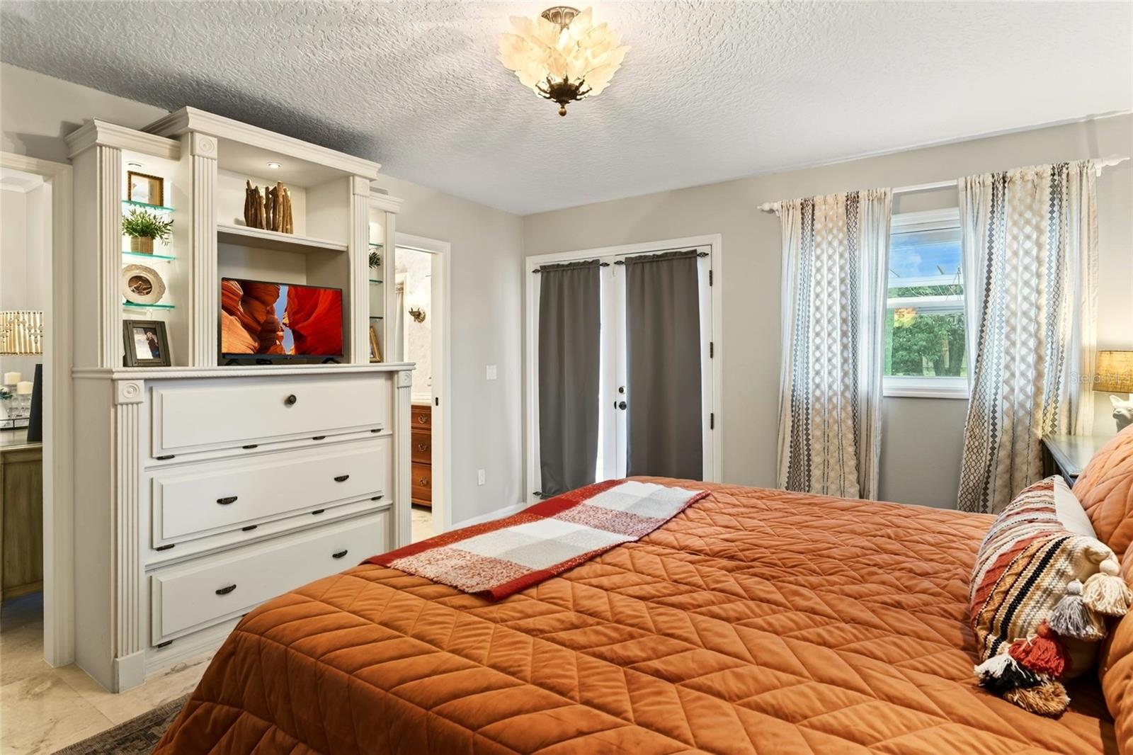 Bedroom with a rust-orange quilted bed, built-in white cabinetry, and curtained doors.