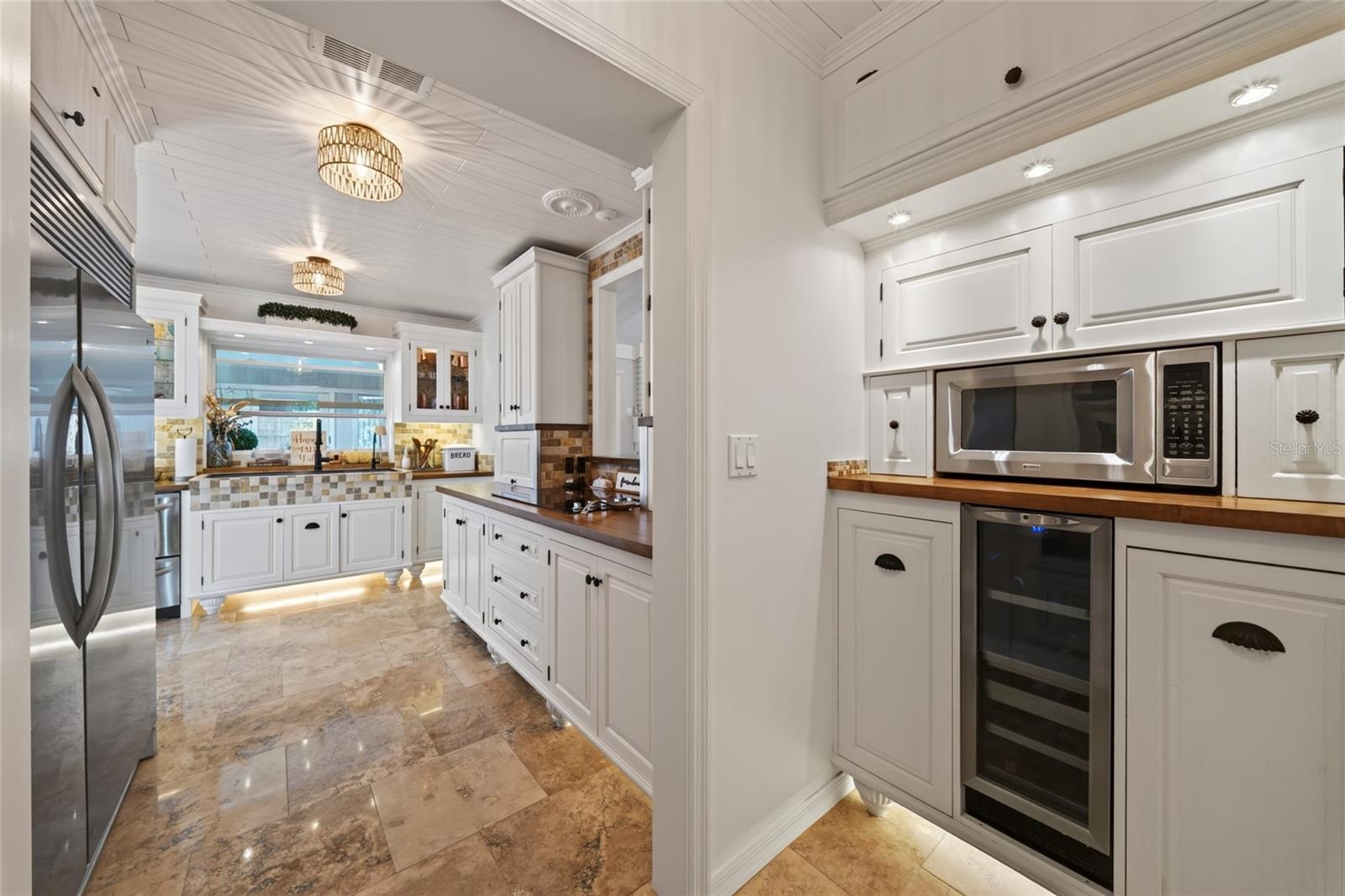 Kitchen with white cabinetry, stainless steel appliances, wood counters, and polished stone tile flooring.