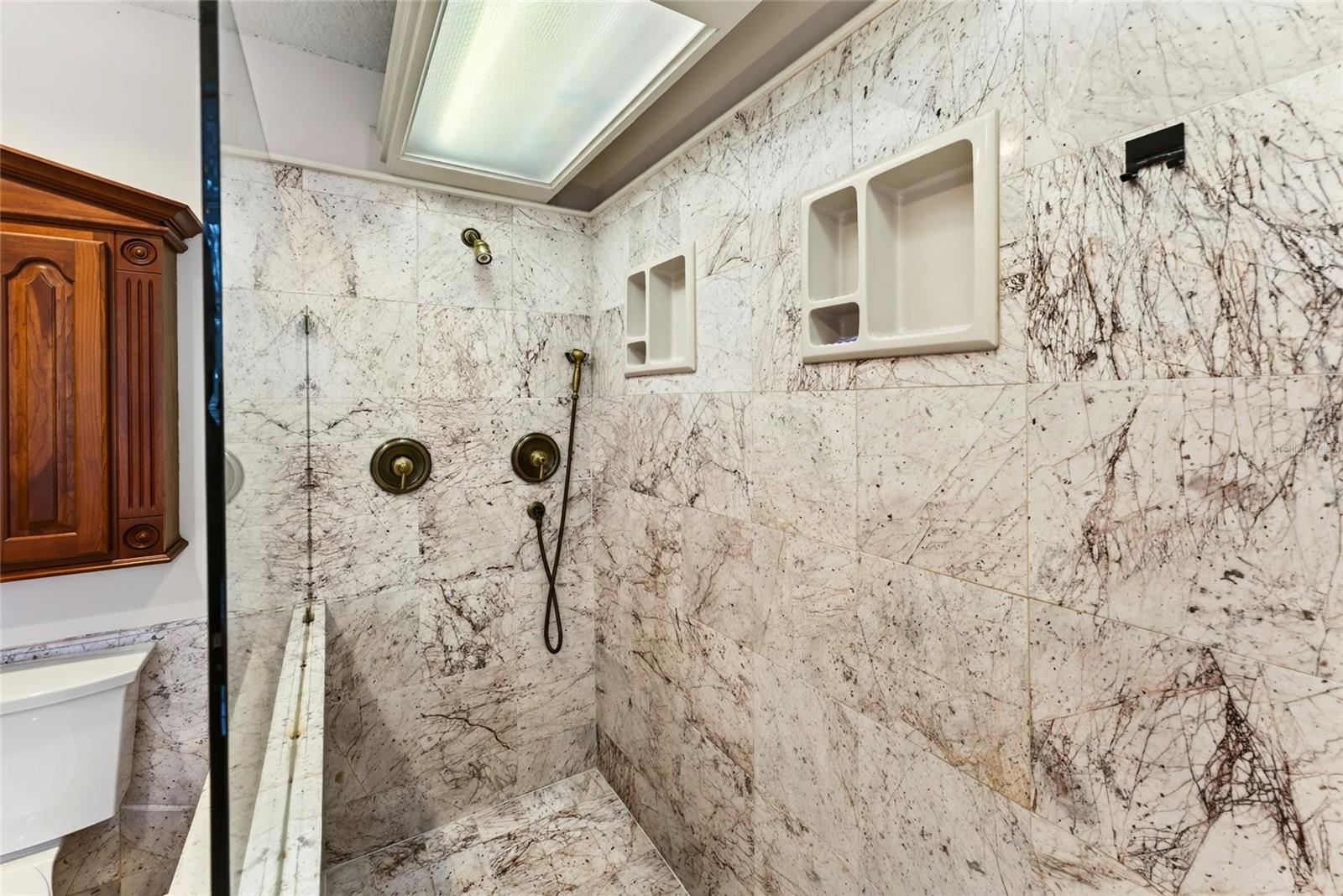 Marble-tiled walk-in shower with brass fixtures and recessed wall niches.