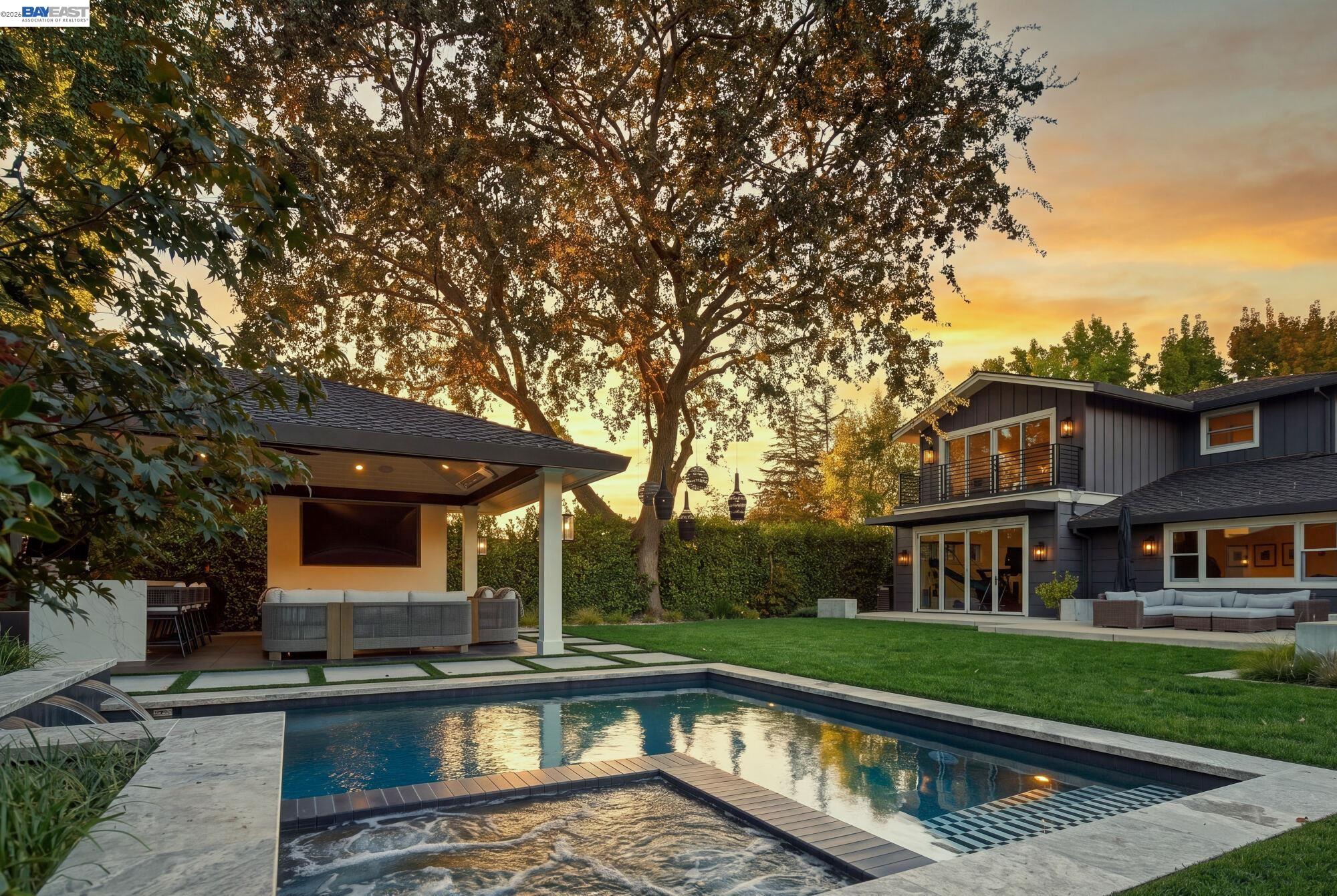 Modern home with a backyard pool, raised spa, and covered outdoor lounge at sunset.