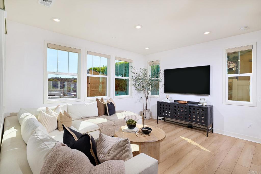 Bright living room with a cream sectional, round wood coffee table, and wall-mounted television.