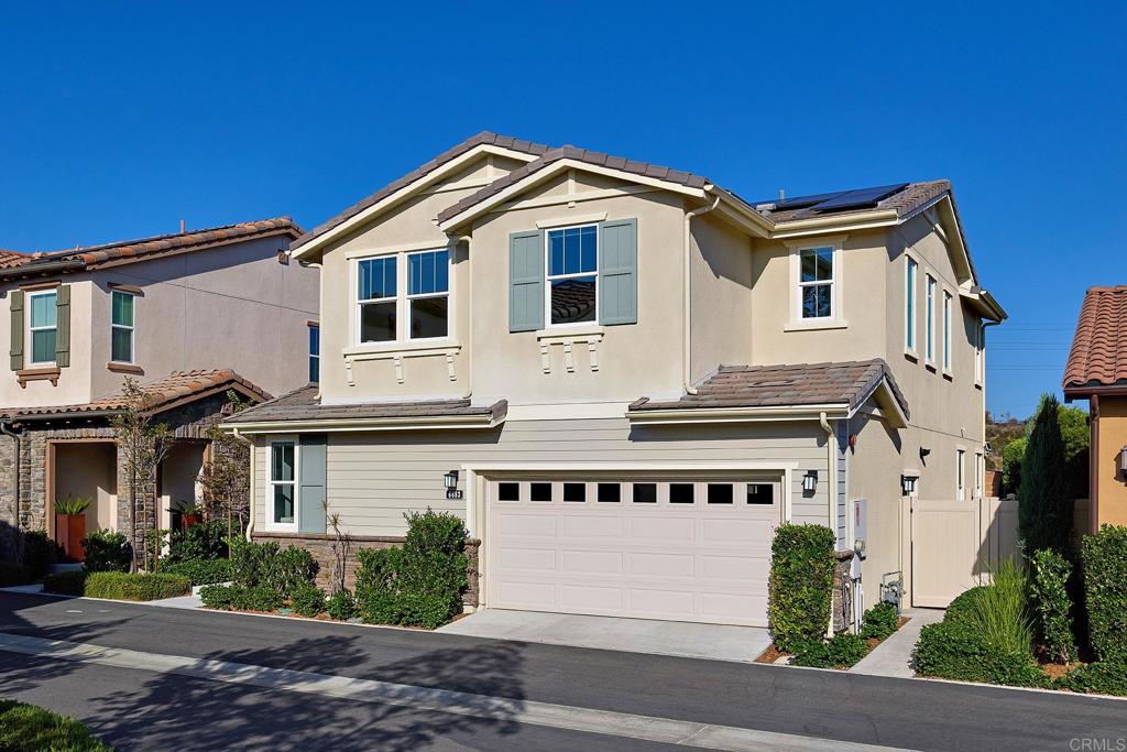 Two-story beige home with pale green shutters, a two-car garage, and solar panels.