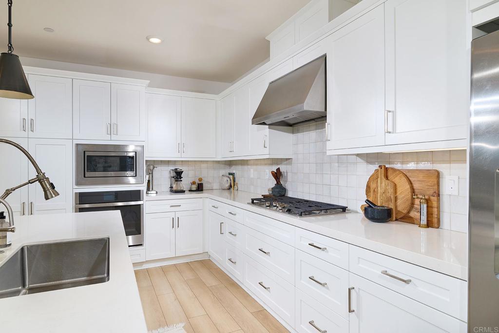 Bright white kitchen with shaker cabinets, stainless appliances, gas cooktop, and light wood flooring.