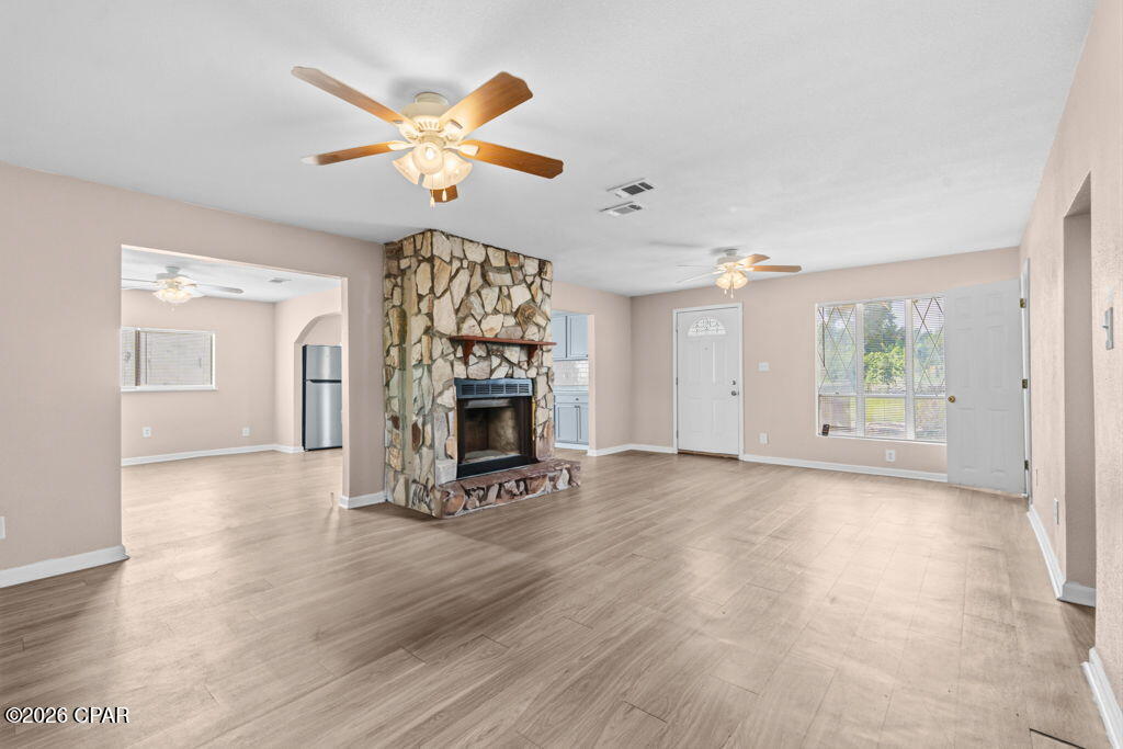 Empty living room with a floor-to-ceiling stone fireplace and light wood-look flooring.