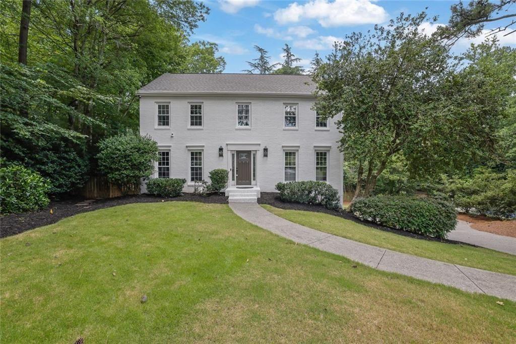 Two-story white house with a curved walkway, broad lawn, and mature trees.