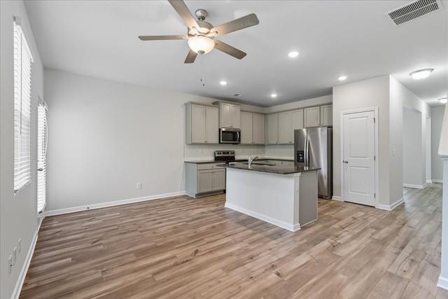 Open-plan kitchen with gray cabinets, stainless steel appliances, and a central island.