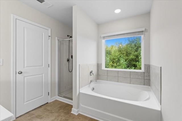 Bathroom with a soaking tub beneath a window overlooking leafy trees, beside a glass-enclosed shower.