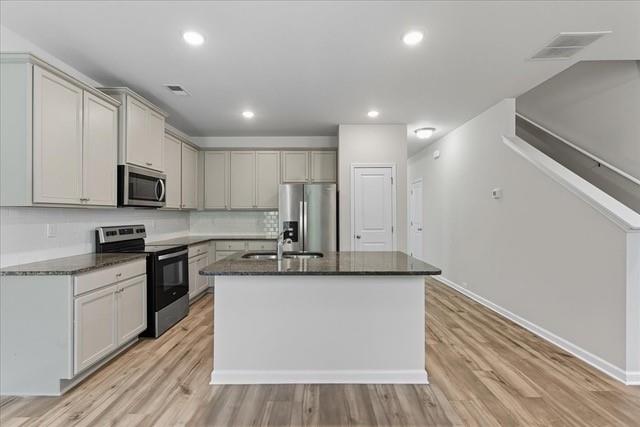 Open-plan kitchen with a central island, white cabinets, stainless steel appliances, and light wood floors.