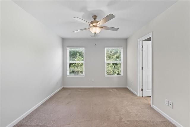 Empty bedroom with beige carpet, two windows, and a ceiling fan with light.
