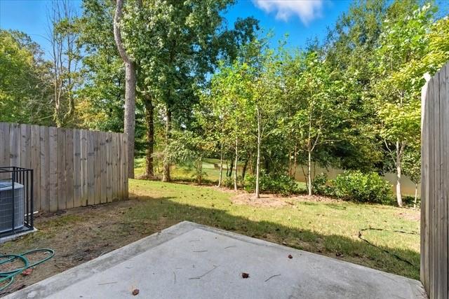 Concrete patio overlooking a grassy, tree-lined backyard enclosed by wooden fencing.