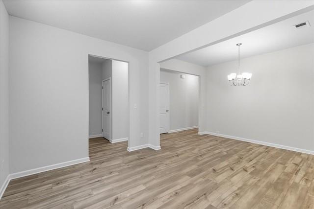 Empty room with wood flooring, a chandelier, and open doorways to adjoining areas.
