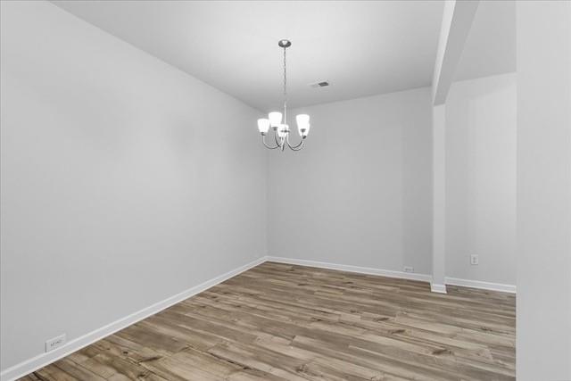 Empty room with wood-look plank flooring and a small chandelier.