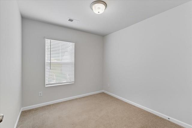 Empty bedroom with beige carpet and a window covered by white blinds.