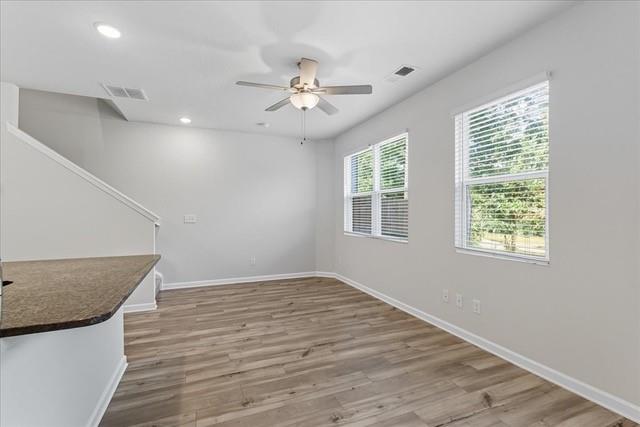 Empty open room with wood-look floors, a ceiling fan, two windows, and a breakfast bar.