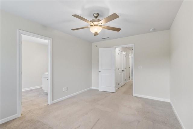 Empty carpeted bedroom with a ceiling fan and open doorways to a bathroom and hall.