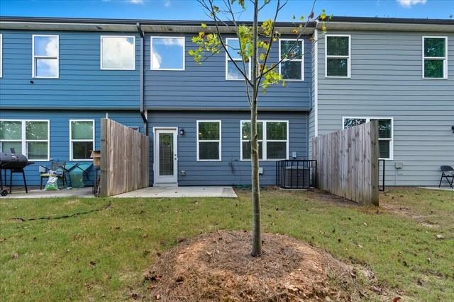 Rear exterior of a blue-sided townhouse with fenced patio and young tree in the yard.