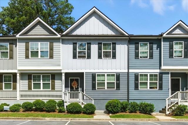 Attached two-story townhomes with gray and white siding, black shutters, and landscaped front shrubs.