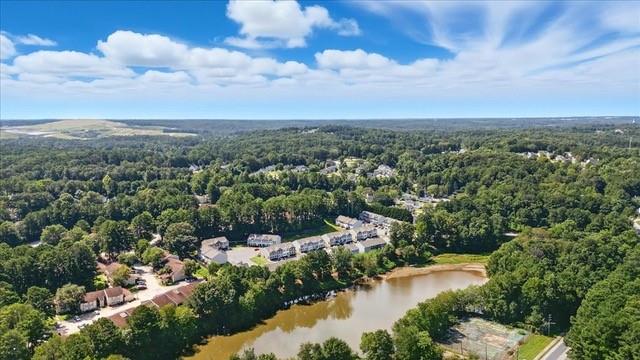 Aerial view of a wooded neighborhood beside a lake under a partly cloudy sky.