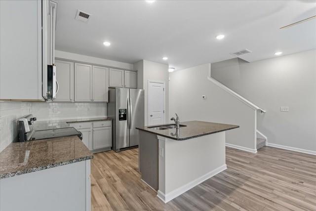 Kitchen with white cabinets, stainless steel appliances, granite countertops, and a central island beside a staircase.