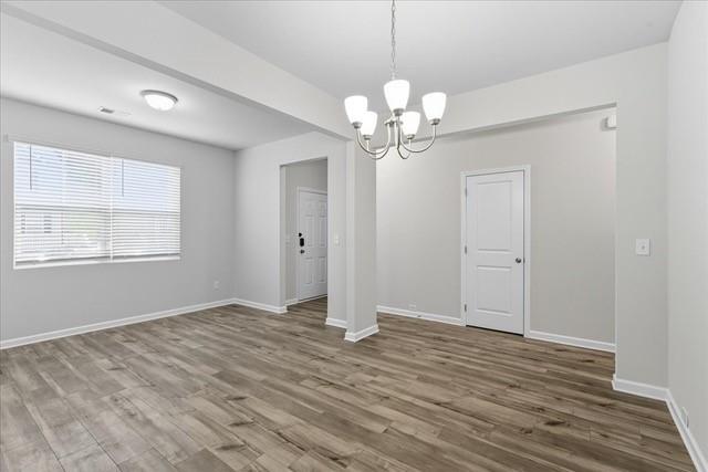 Vacant dining room with wood-look flooring, chandelier, and a large window with blinds.
