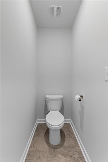 Narrow bathroom with a white toilet and brown stone-look tile floor.