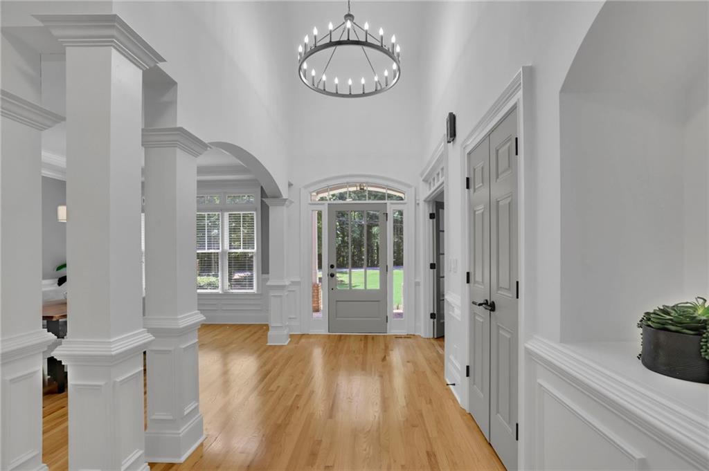 Foyer with hardwood floors, a round chandelier, white paneled walls, and a glass-paneled front door.