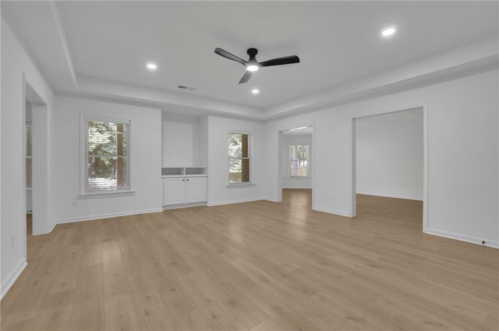 Open living area with light wood floors, a ceiling fan, and built-in cabinetry.