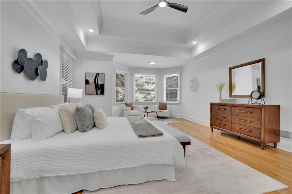 Staged bedroom with a white bed, tray ceiling, and bay windows.