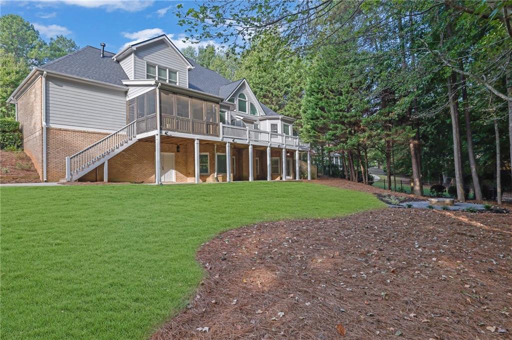Rear of a two-story house with a raised deck and screened porch overlooking a green lawn.