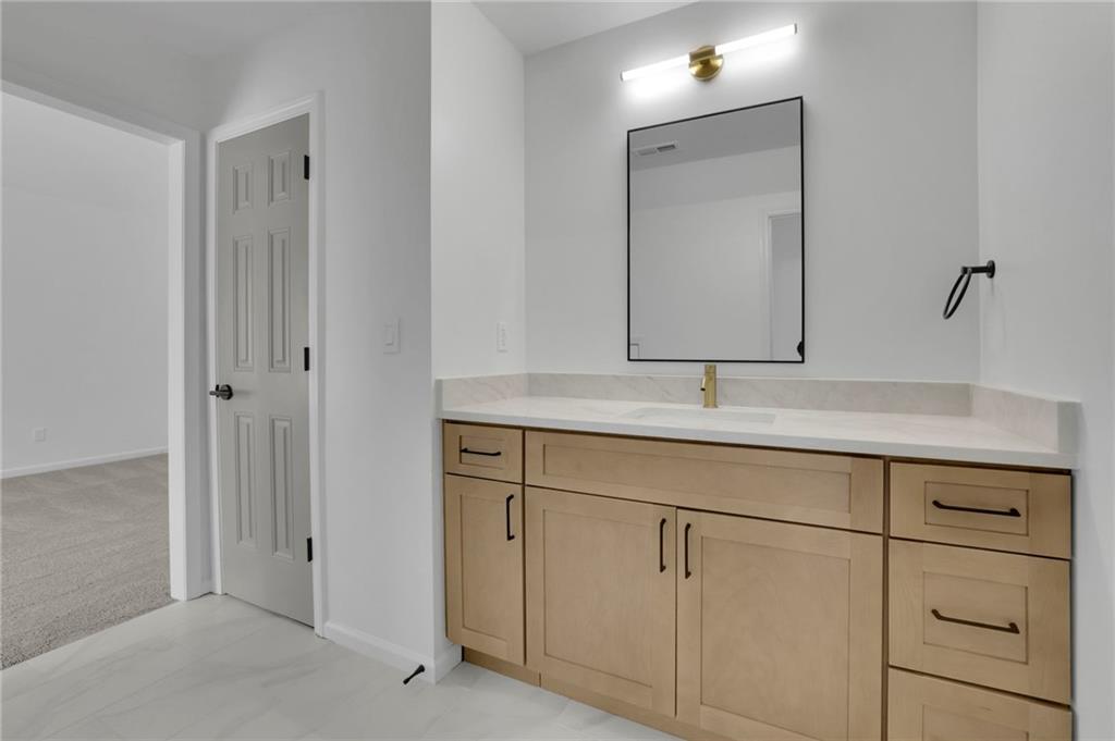 Bathroom vanity with light-wood cabinetry, a white counter, brass faucet, and large mirror.