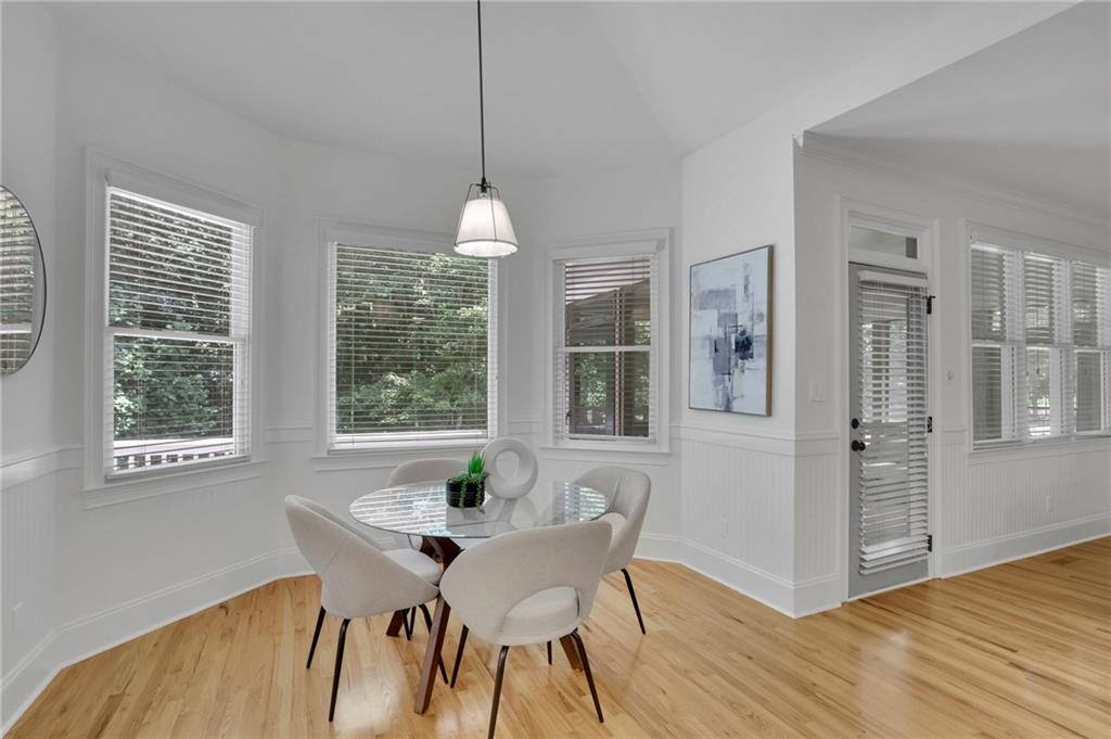 Dining nook with a glass-top table, upholstered chairs, and multiple windows with blinds.