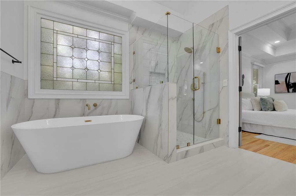 Marble bathroom with a freestanding tub, leaded-glass window, and glass-enclosed shower.