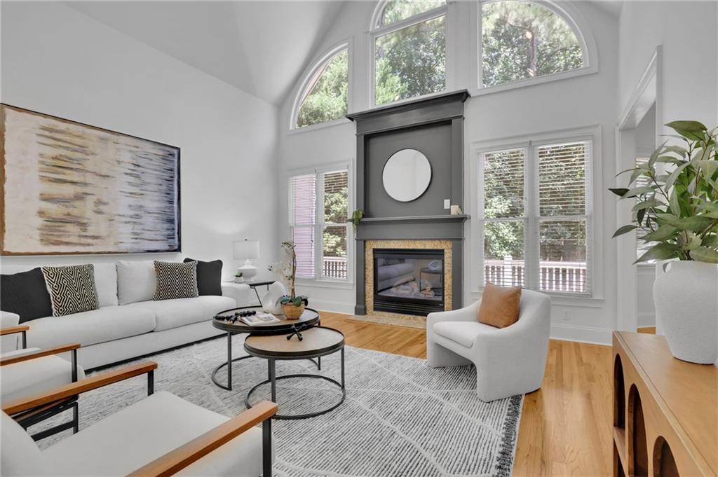 Furnished living room with a tall fireplace, vaulted ceiling, and arched windows.