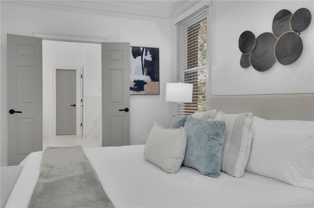 Staged bedroom with a white bed, pale blue pillows, gray doors, and circular metal wall decor.
